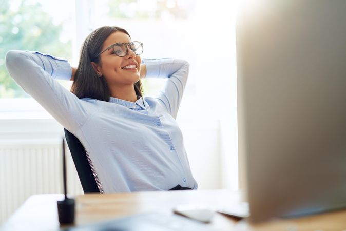 Confident female sitting at her desk relaxing with her hands behind her head