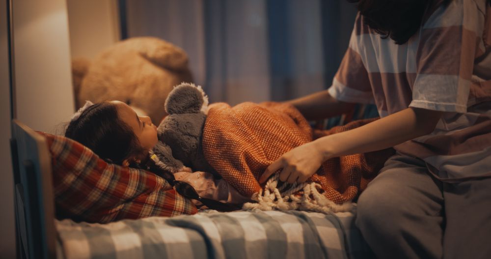 Korean Young Mother Caring for Her Lovely Daughter, Putting Her to Sleep in Bed at Home in the Evening.