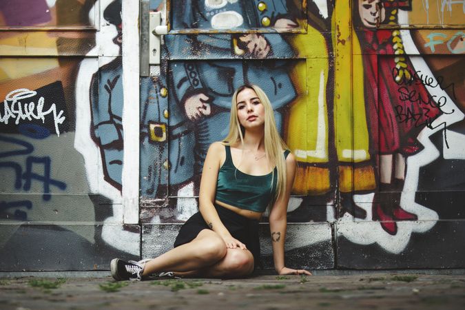 Stylish woman in sunglasses posing at graffiti wall on city street.