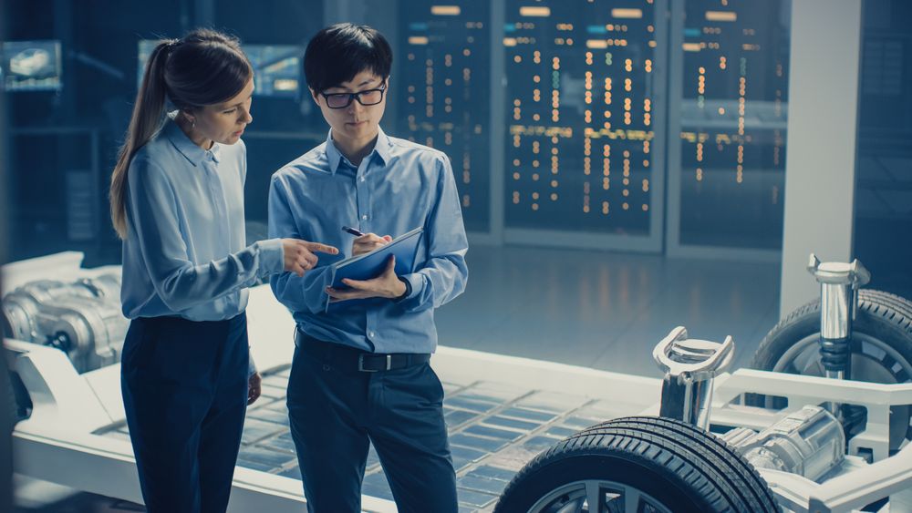 Male and Female Automobile Design Electric Car Engineers Having Conversation, Use Clipboard to Check Maintenance Issues.