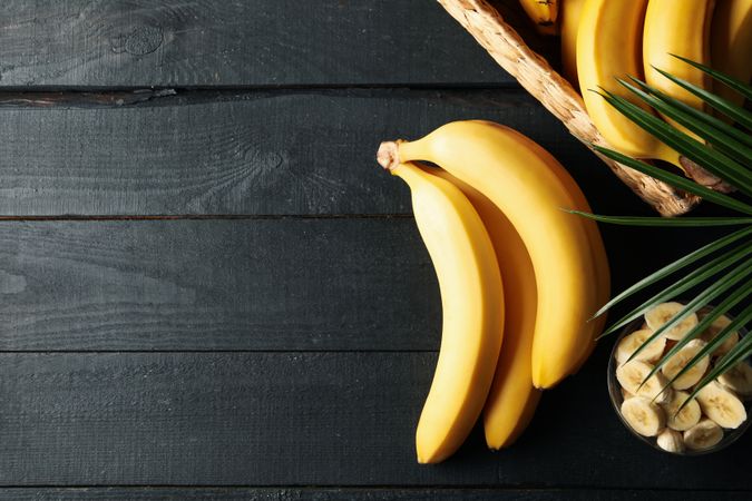 Bananas. Basket with bananas and bowl with slices on wooden background