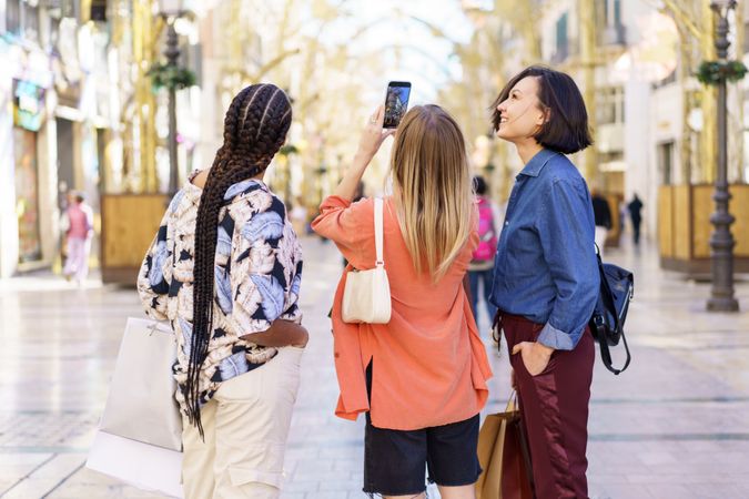 Three women looking up while taking picture on street with phone