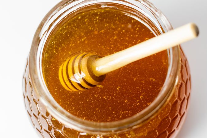 Dipper stirring fresh aromatic golden honey in glass jar