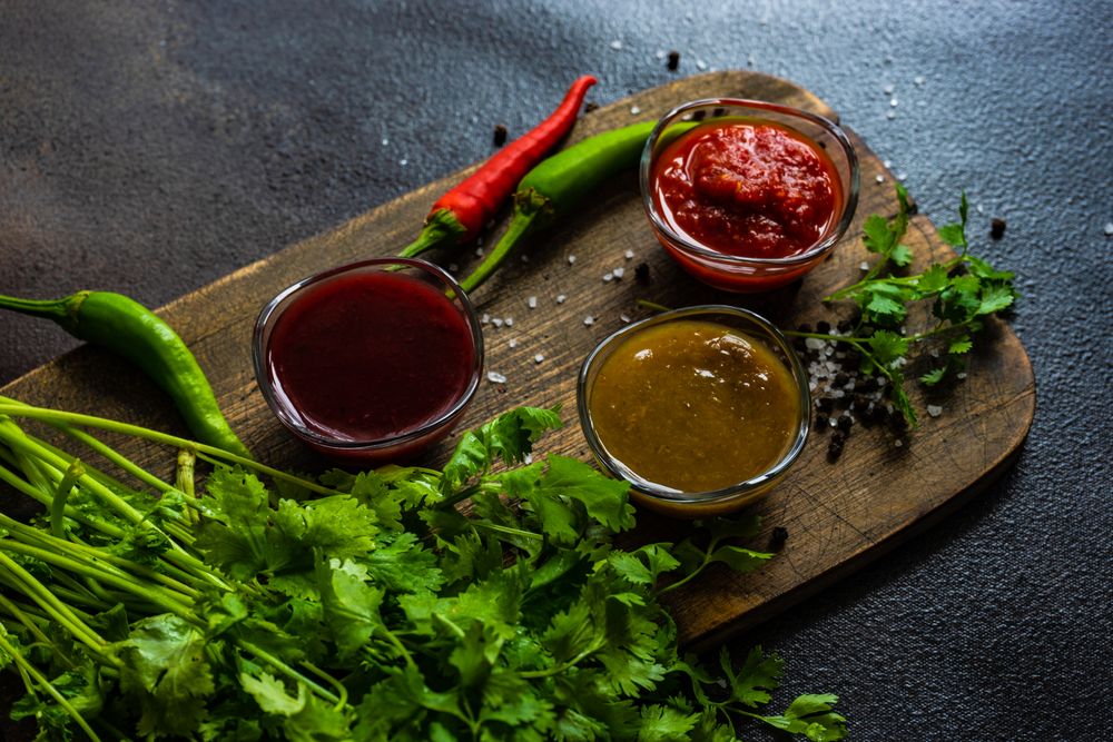 Three traditional Georgian condiments tomato satsebeli, yellow and red tkemali with ingredients on wooden board