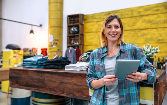 Portrait of smiling blonde young female entrepreneur looking at camera in front of shop counter