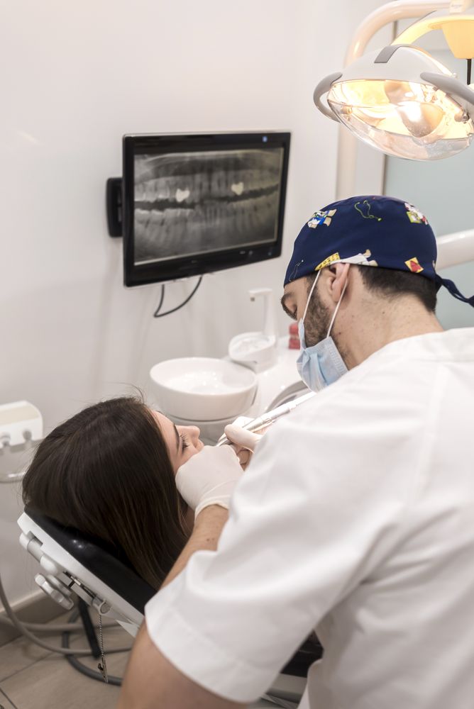 Back of male dentist drilling tooth in female patient