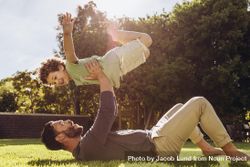 Man lying on ground and lifting his son with his arms in a park 5zZRA5