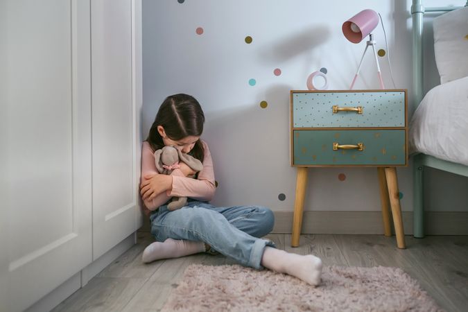 Sad girl hugging stuffed toy sitting on the floor
