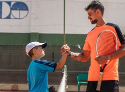Father and son playing tennis together on a dirt court