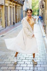 Happy fashionable woman standing in street with long coat and geometric dress