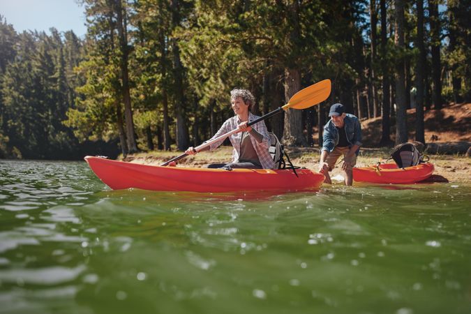 Portrait of mature woman canoeing in the lake with man about to catch the kayak from behind