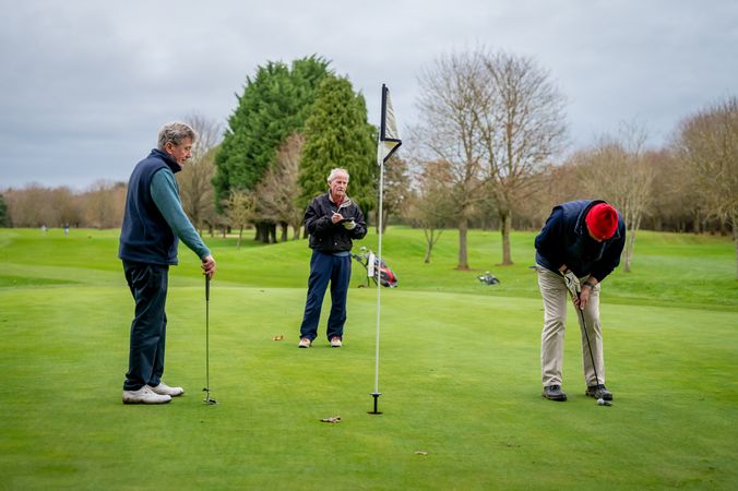 Man putting towards hole with friends looking on on golf course