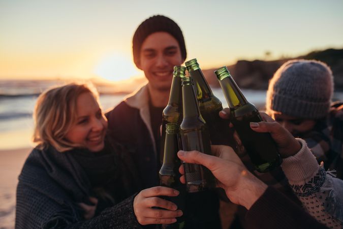 Young people toasting with beer bottles on beach