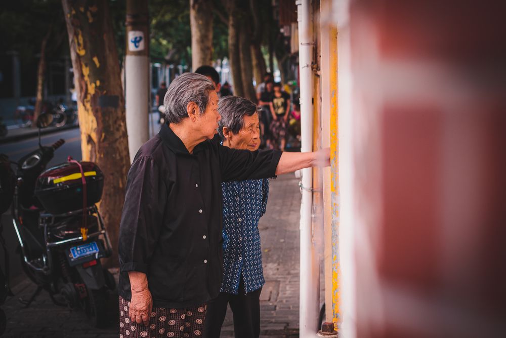 Side view of two older people standing on sidewalk