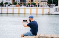 Guy on vacation in casual clothing making photo of bay on smartphone at quay