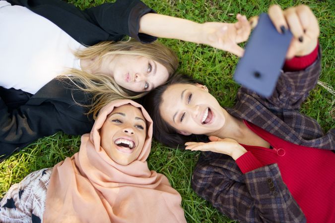 Looking down at three women lying back on grass with smartphone