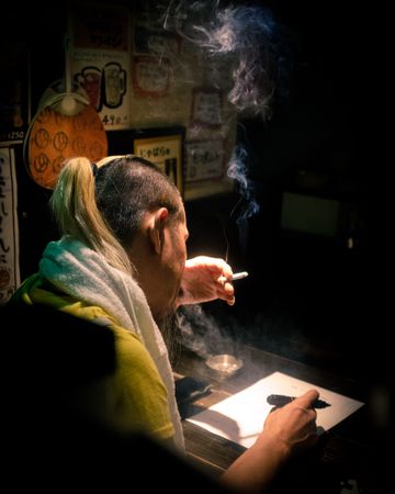 Back view of man smoking cigarette while writing