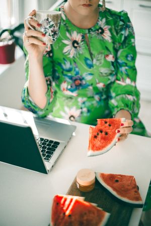 Woman working on her laptop and eating watermelon