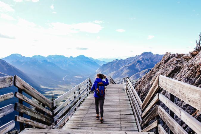 Back view of person with backpack walking on wooden bridge in the mountains