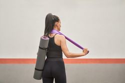 Female athlete in sportswear standing with yoga mat and resistan