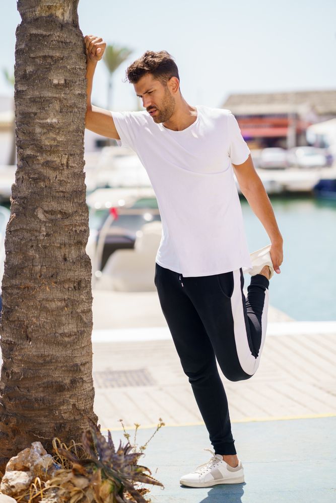 Man balancing next to palm tree as he stretches his quads