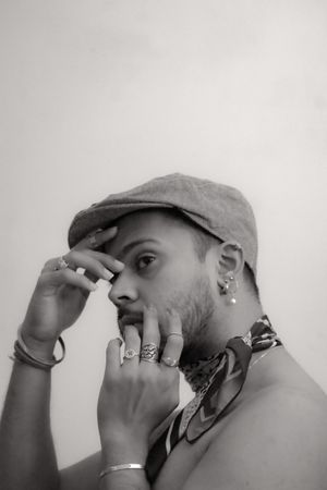 Grayscale photo of topless man wearing hat and jewelry