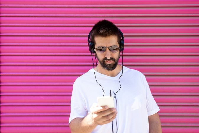 Latino man in headphones checking phone in front of pink wall