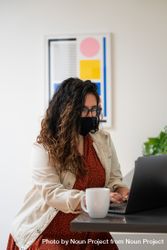 Woman with long curly hair working on a laptop wearing a face mask 0gaV74