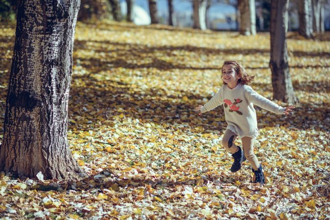 Playful girl running in park of colorful fall leaves with her arms open