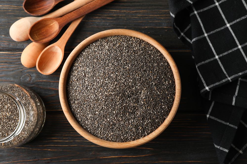 Chia in wooden bowl on wood background, top view