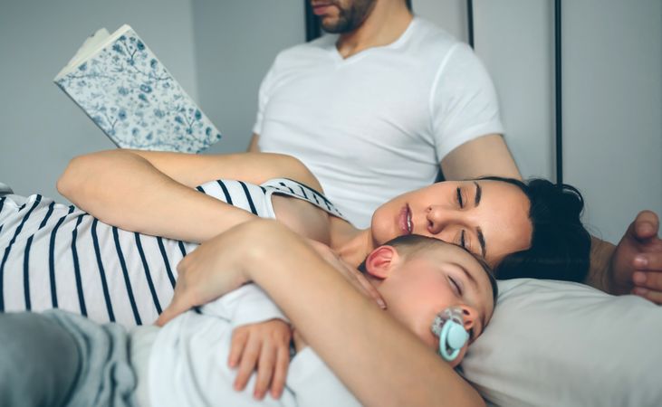 Man reading with wife and son sleeping