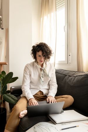 Woman using laptop near draws on papers on sofa in room