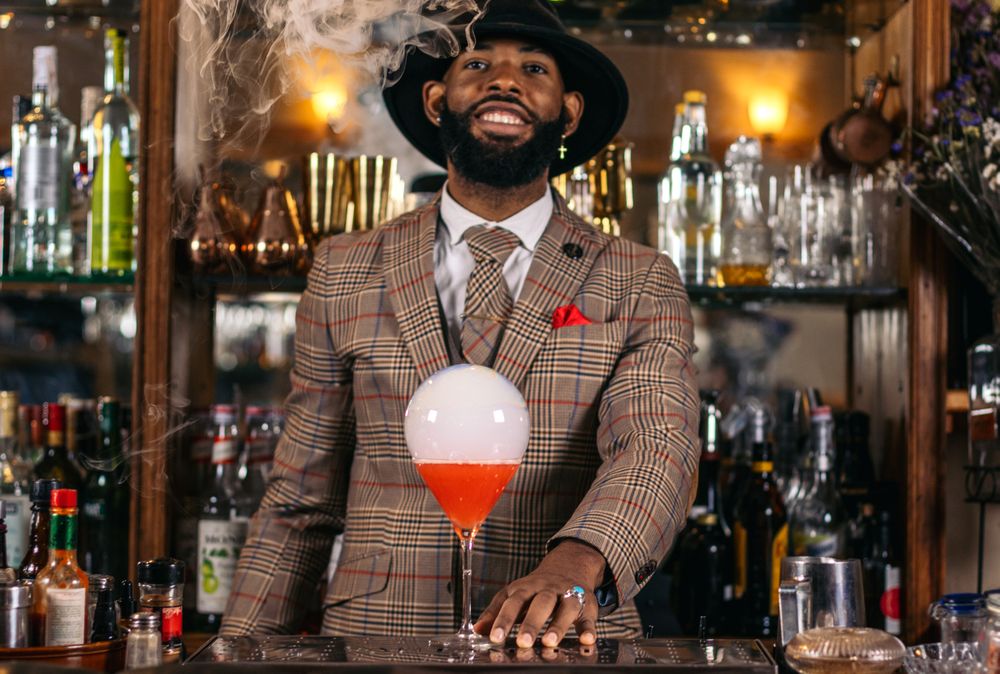 Stylish Black bartender preparing a cocktail with a smoke bubble in a traditional cocktail bar