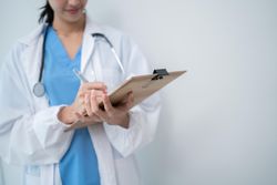 Mid shot of doctor standing in bright hospital room writing in clipboard with copy space