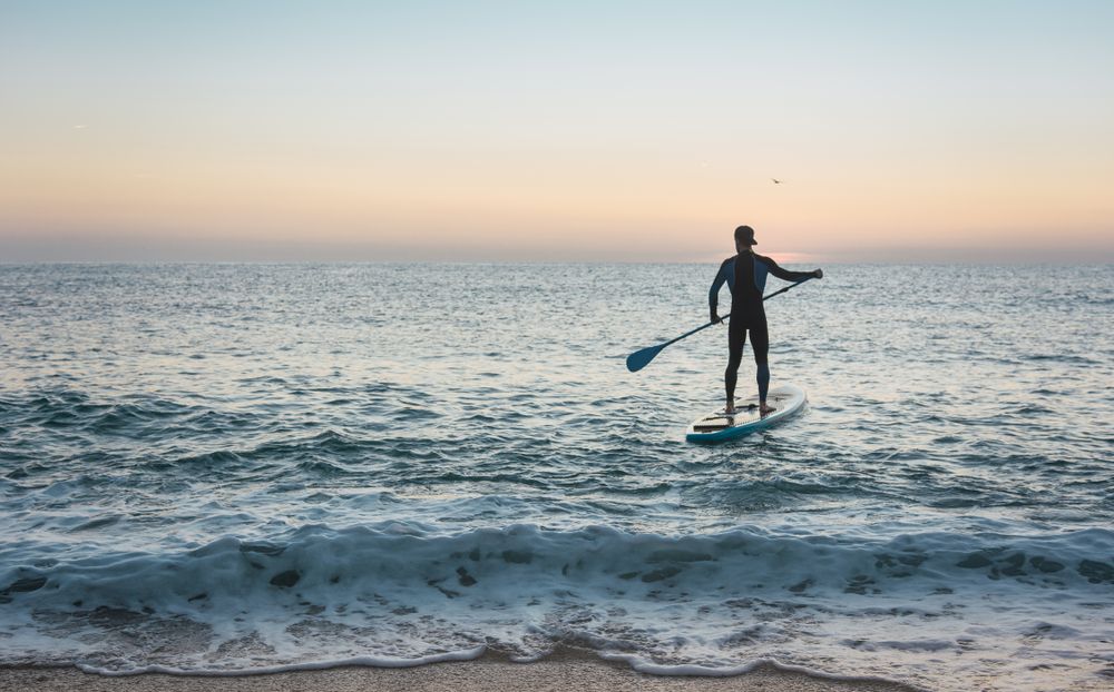 Man practicing paddle surfing with neoprene in a sunrise