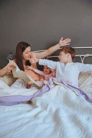 Portrait of mother playfully reading book to her daughter and son in bed