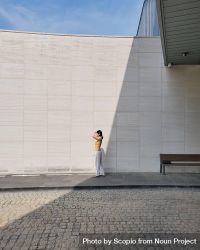 Woman standing on sidewalk beside light wall 4BYG35
