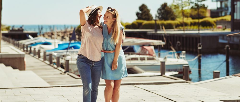 Women smiling and strolling together on sunny day near the river