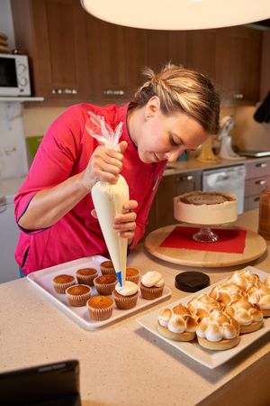 Female confectioner decorating cupcakes using piping bag