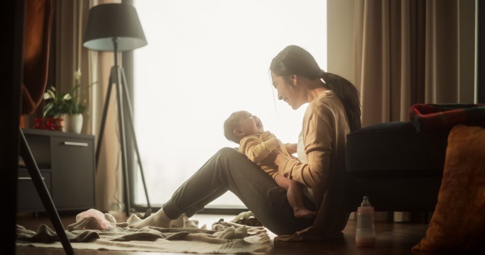 Mother and Baby Bonding Moment: Authentic Shot of an Asian Woman New to Motherhood Playing with her Cute Child in the Morning at Home.