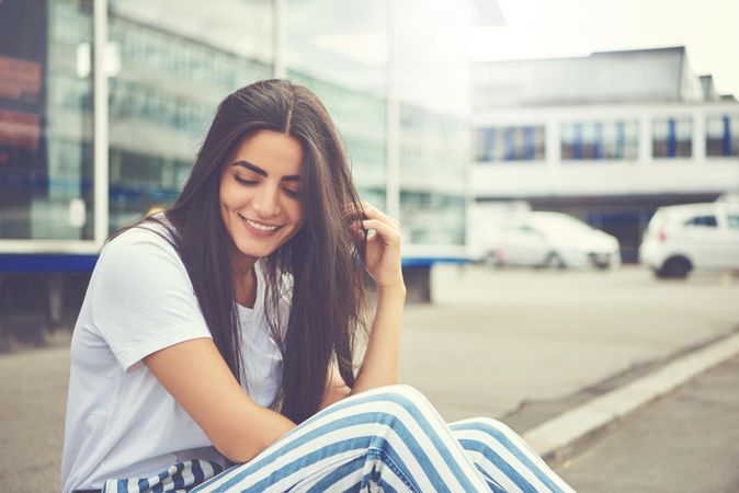 Happy woman sitting on curb running her fingers through her hair