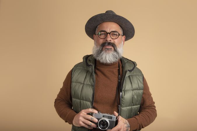 Bearded man holding a camera standing against yellow background