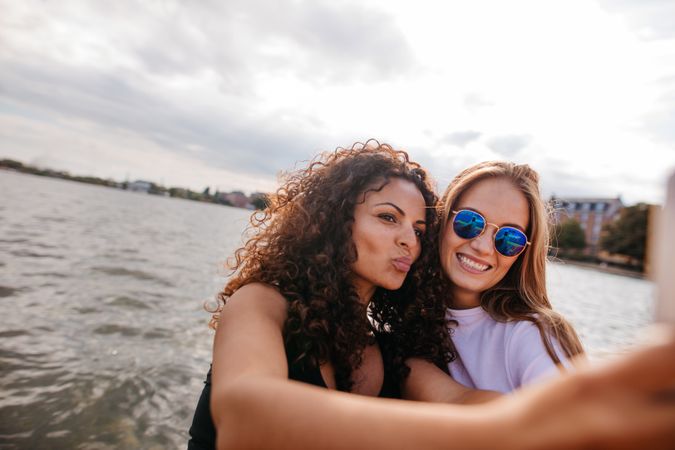 Two female friends taking selfie with mobile phone by the lake