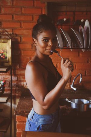 Woman wearing dark bra eating with spoon standing in the kitchen
