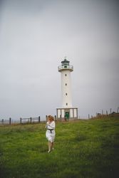 Woman running in green meadow near lighthouse