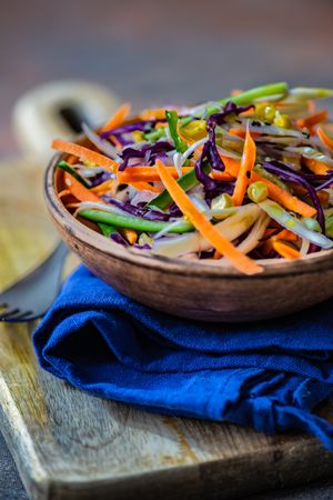 Close up of fresh salad with vegetables in bowl on wooden board with copy space