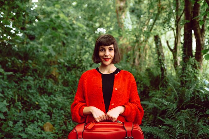 Woman in red with big red suitcase in forest