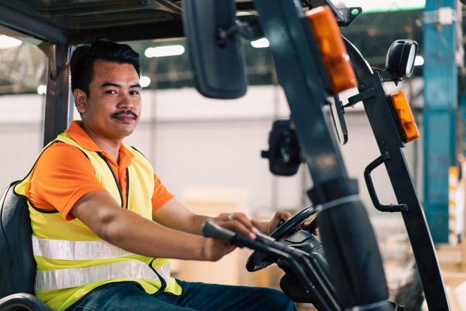 Man in high visibility vest driving forklift in factory