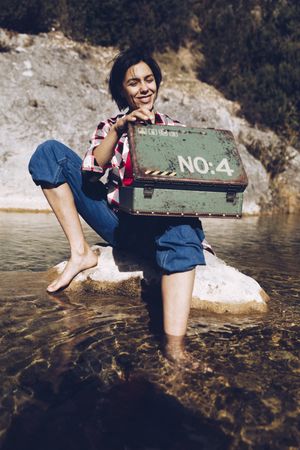 Woman with picnic case on rock in water