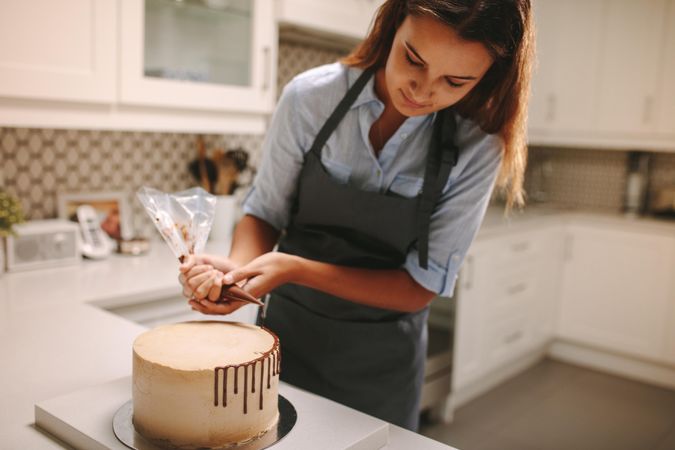 Young woman decorating cake with chocolate